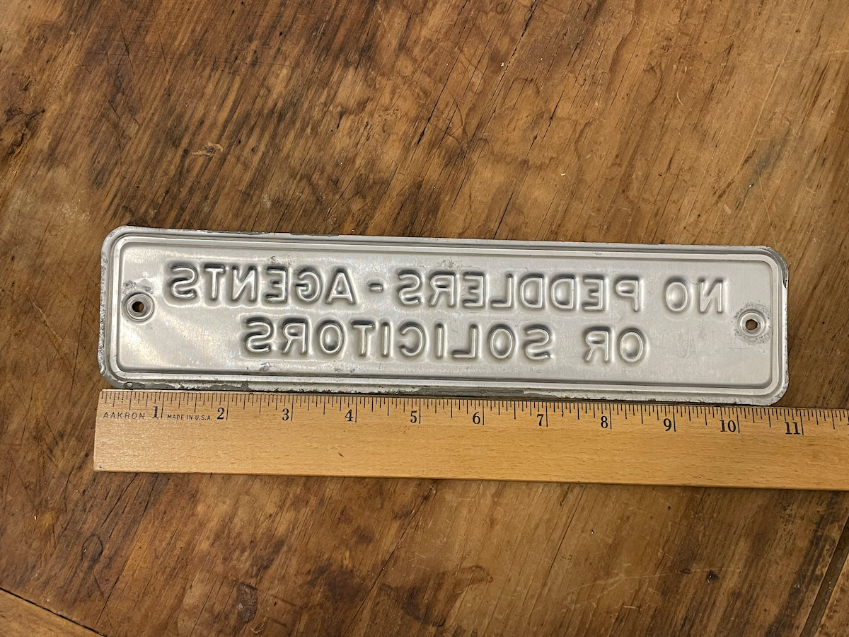 Metal sign with engraved text on a wooden surface with a ruler for scale.