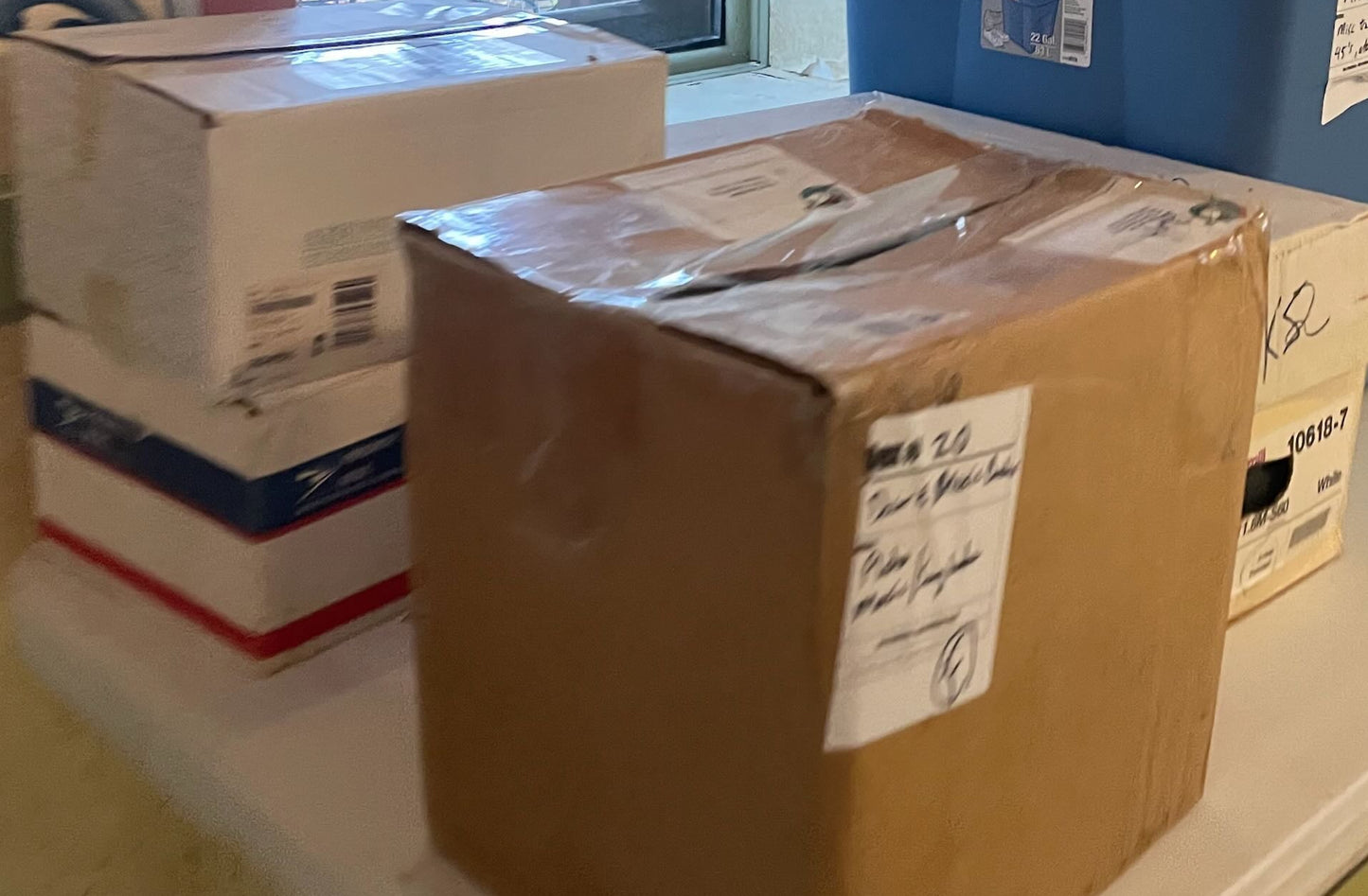 Stack of boxes on a table near a window with a colorful painting in the background.