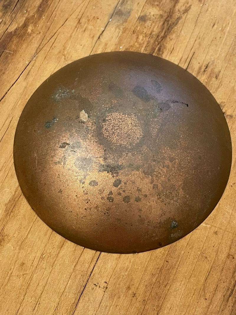 Underside of copper bowl against a wooden surface