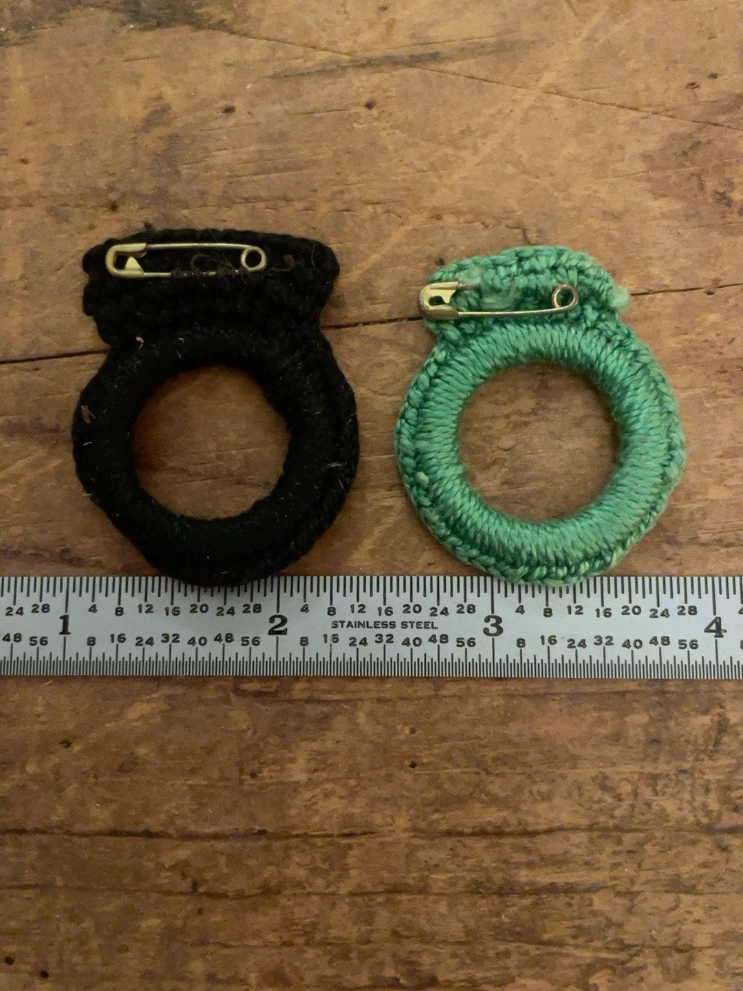Backs of vintage fiber-wrapped ring pins showing safety pins and ruler for scale