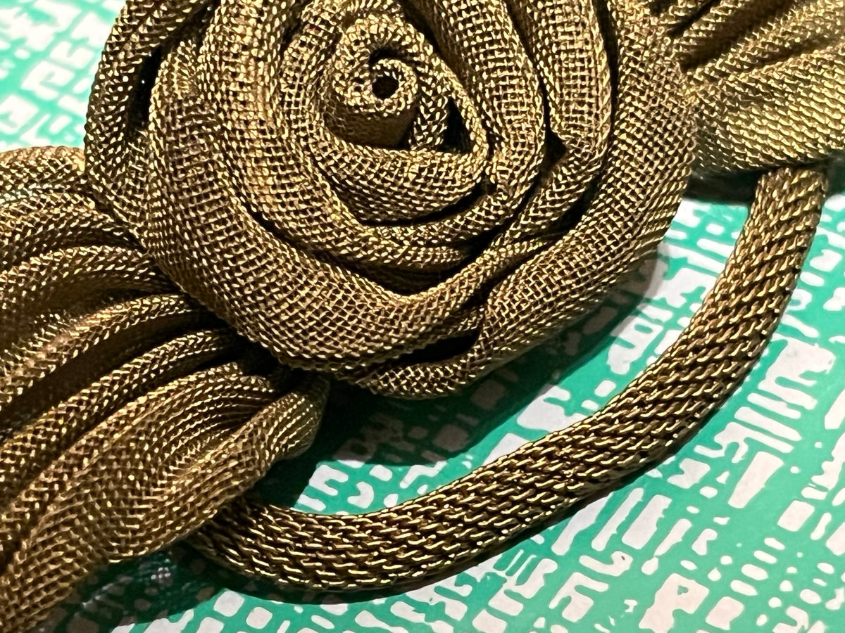 Close view of sculptural rose formed from flexible woven gold-tone metal mesh