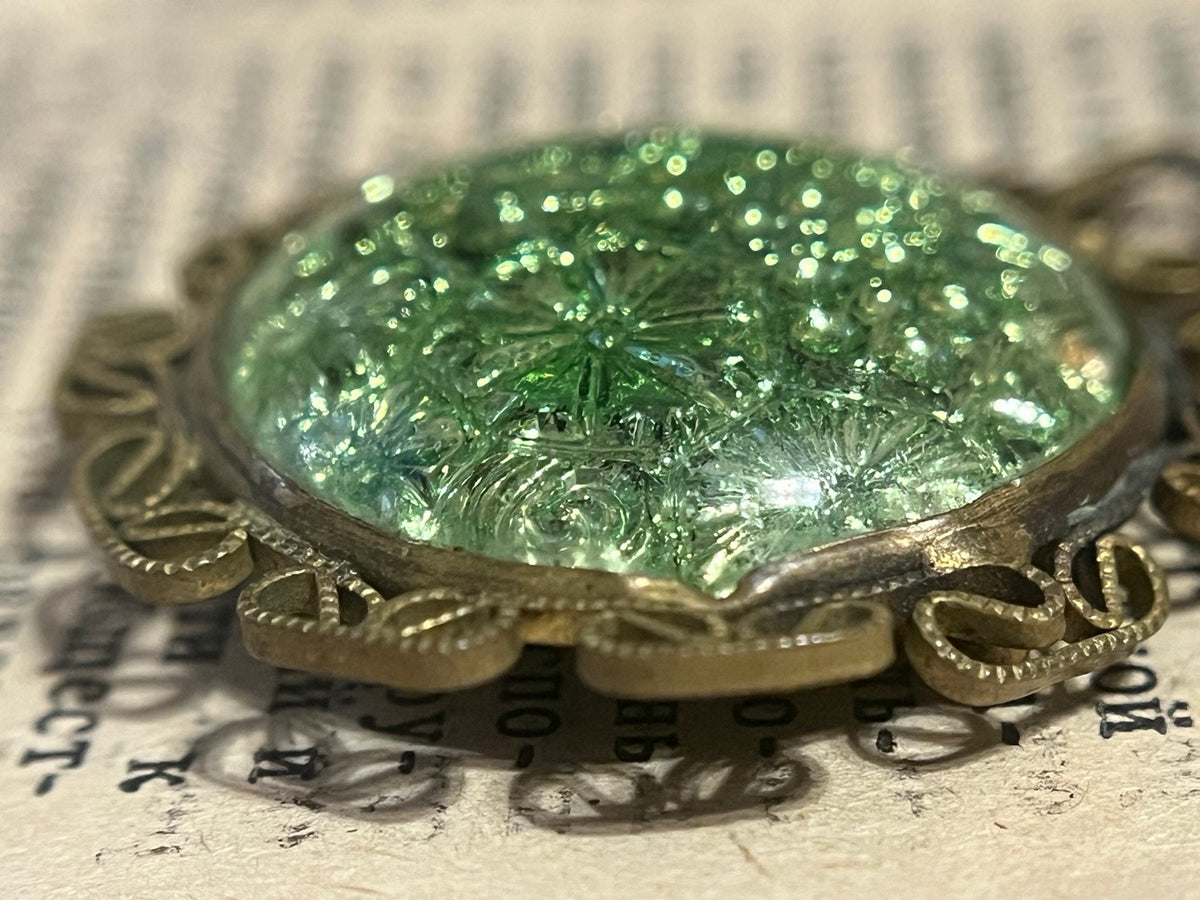 Profile view of molded iridescent floral glass in ornate metal filigree setting
