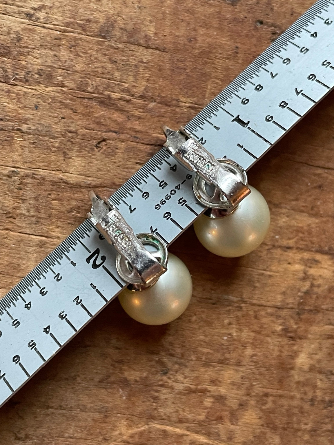 Backs of vintage Crown Trifari faux pearl clip-on earrings showing maker marks