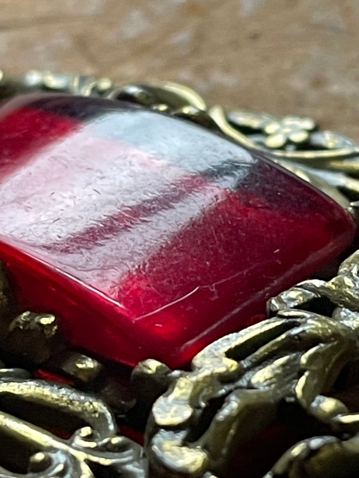 Close-up of red glass cabochon and gold-tone setting showing vintage surface wear