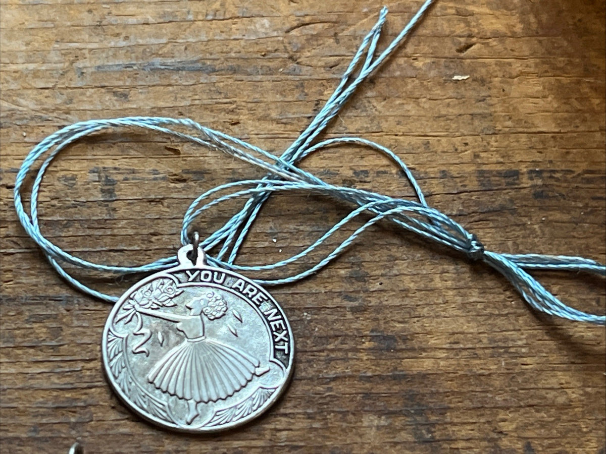 Round silver-tone You Are Next charm tied to a pale blue cord