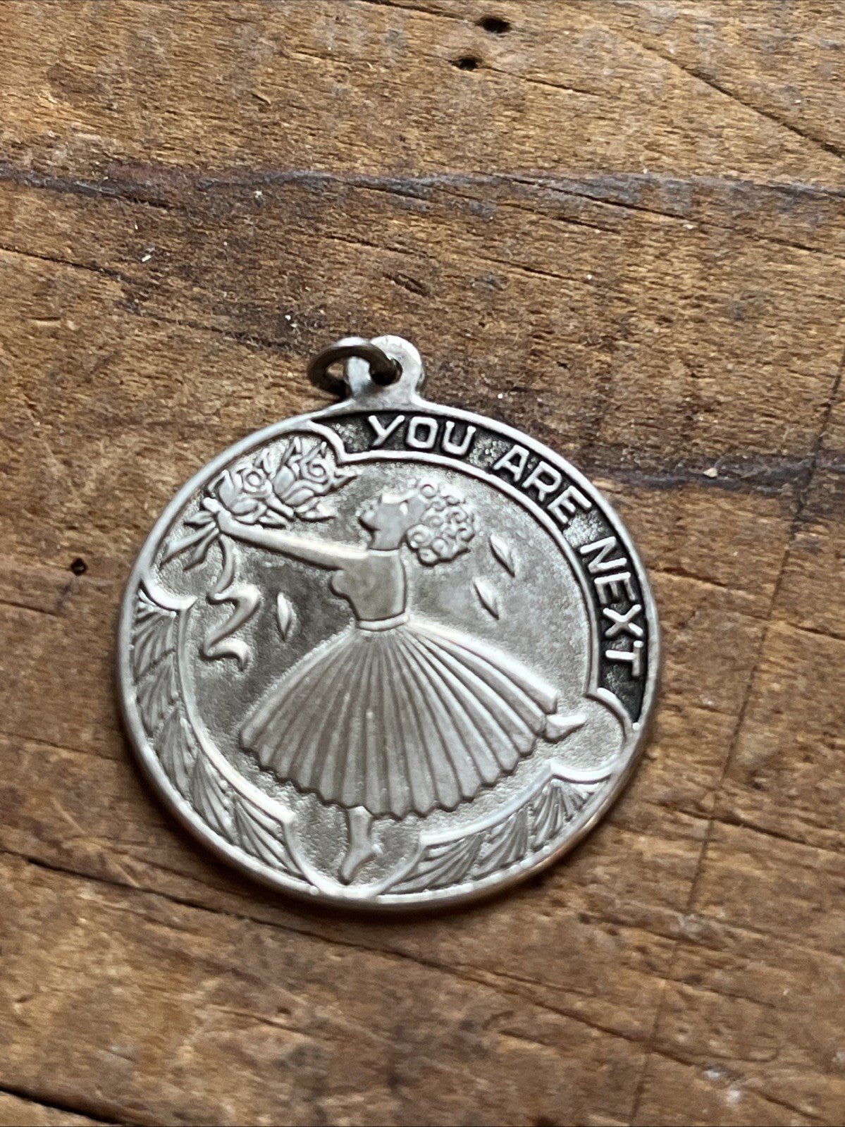 Round bridal charm with a bouquet design and You Are Next lettering