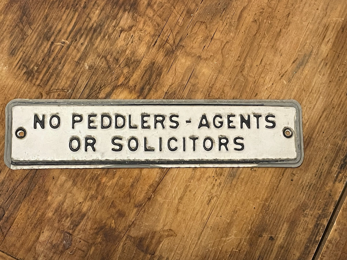 Metal sign on a wooden surface reading 'No Peddlers - Agents or Solicitors'.