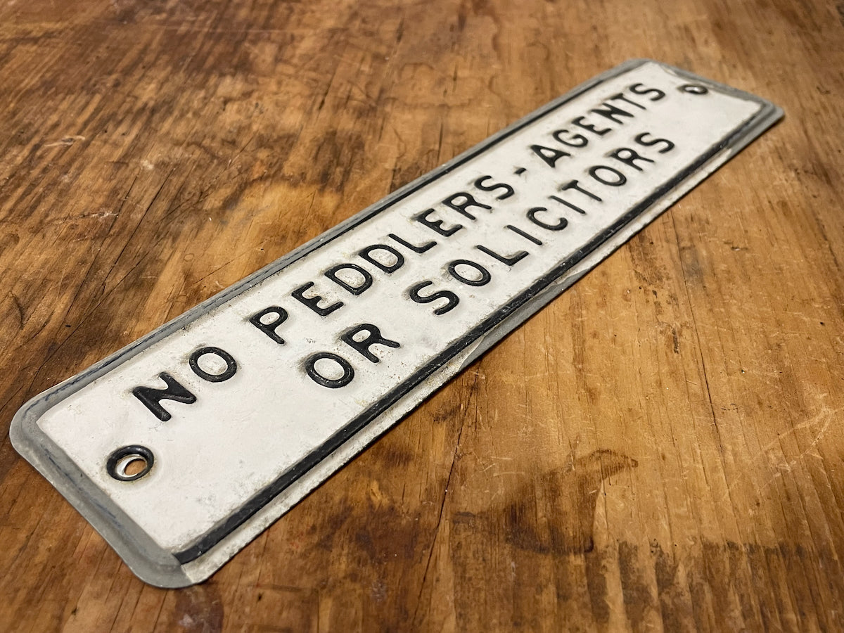 Metal sign on a wooden surface with text 'No Peddlers, Agents or Solicitors'.