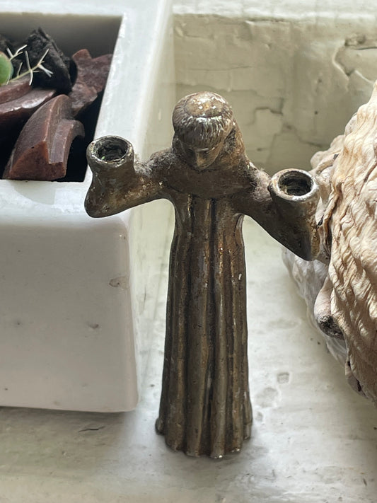 Front view of small vintage cast metal monk or saint figure with upheld arms 