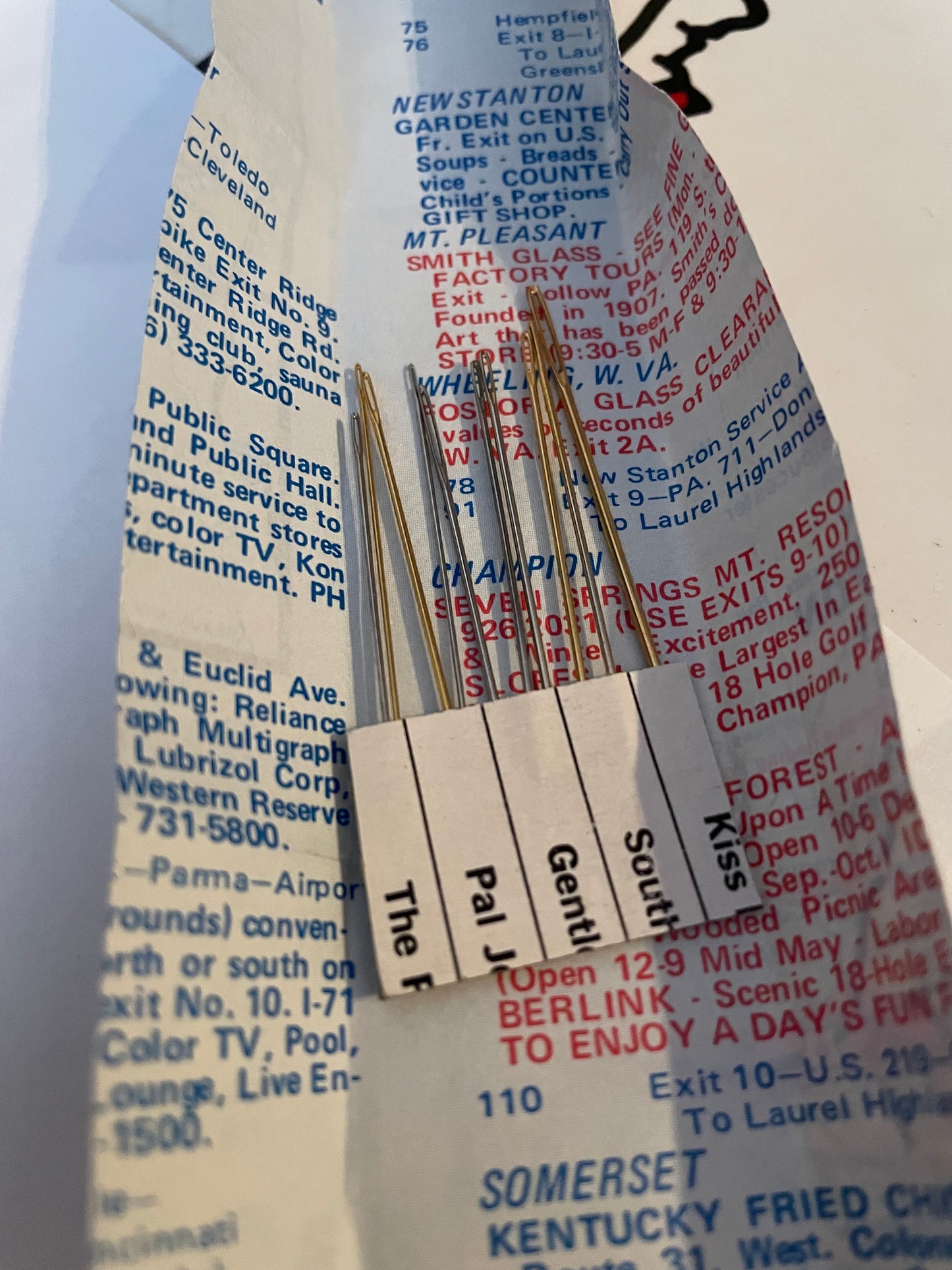 ten hand sewing needles in open packaging (the back side of a page from a travel map).