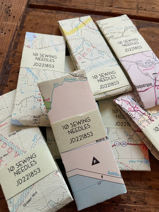 a few packets of packaged 'ten sewing needles' product against a weathered wood background