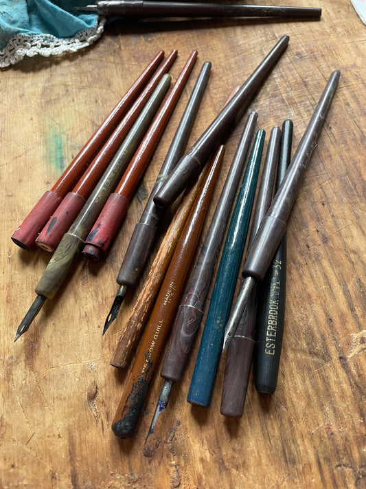 Collection of various crow quill dip penholders on a wooden surface