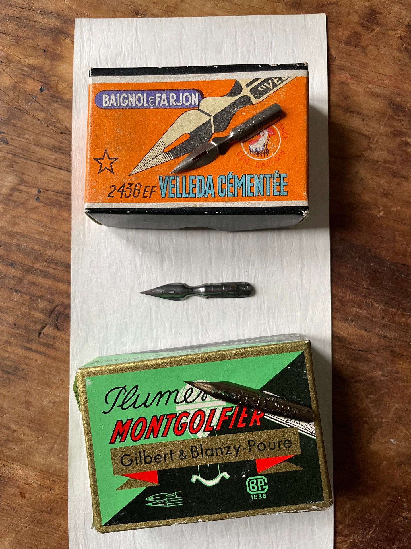 two vintage boxes and 3 metal writing nibs against a wooden surface.