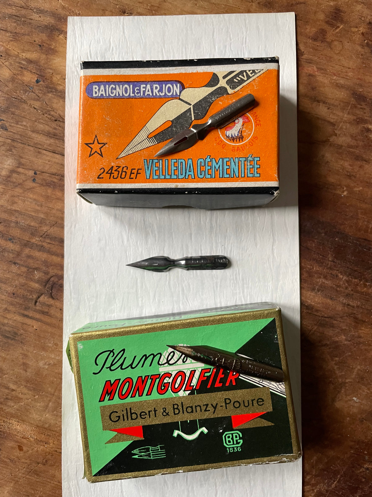 two vintage boxes and 3 metal writing nibs against a wooden surface.