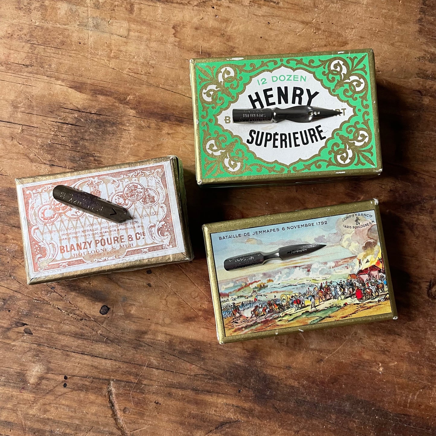 Three vintage boxes of antique french writing nibs, with a nib of each style displayed on a wooden surface