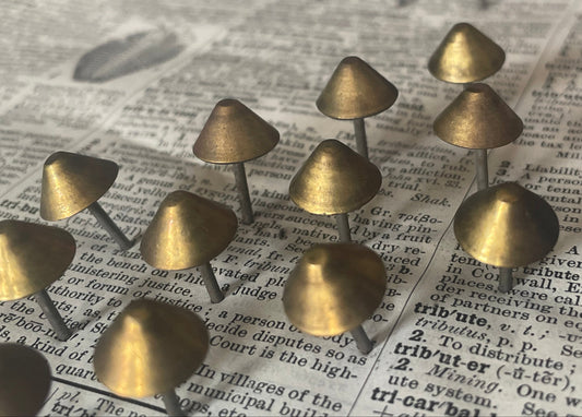 A group of small metallic mushroom-shaped upholstery studs with tapered bronze-colored tops and thin stems, arranged on an open book with printed text.