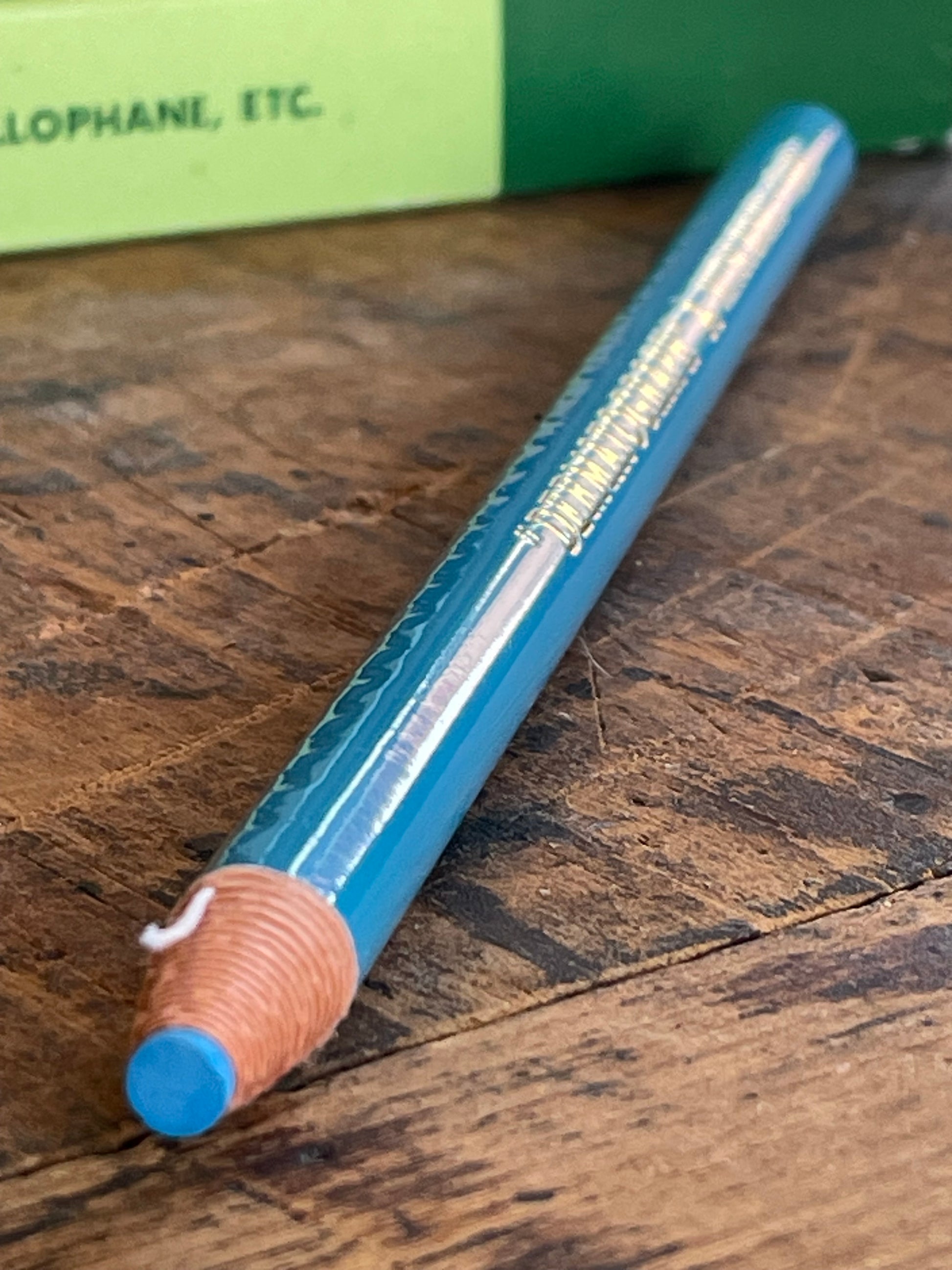 A blue dermatograph pencil with its string showing through the unused pencil end, resting diagonally on a rustic wooden surface.