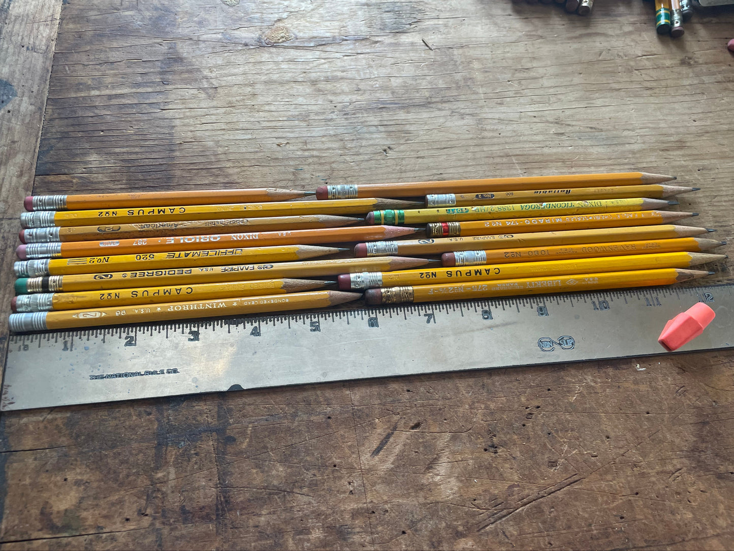 A group of yellow wooden pencils with erasers and erasers laid next to a metal ruler on a rustic wooden tabletop.