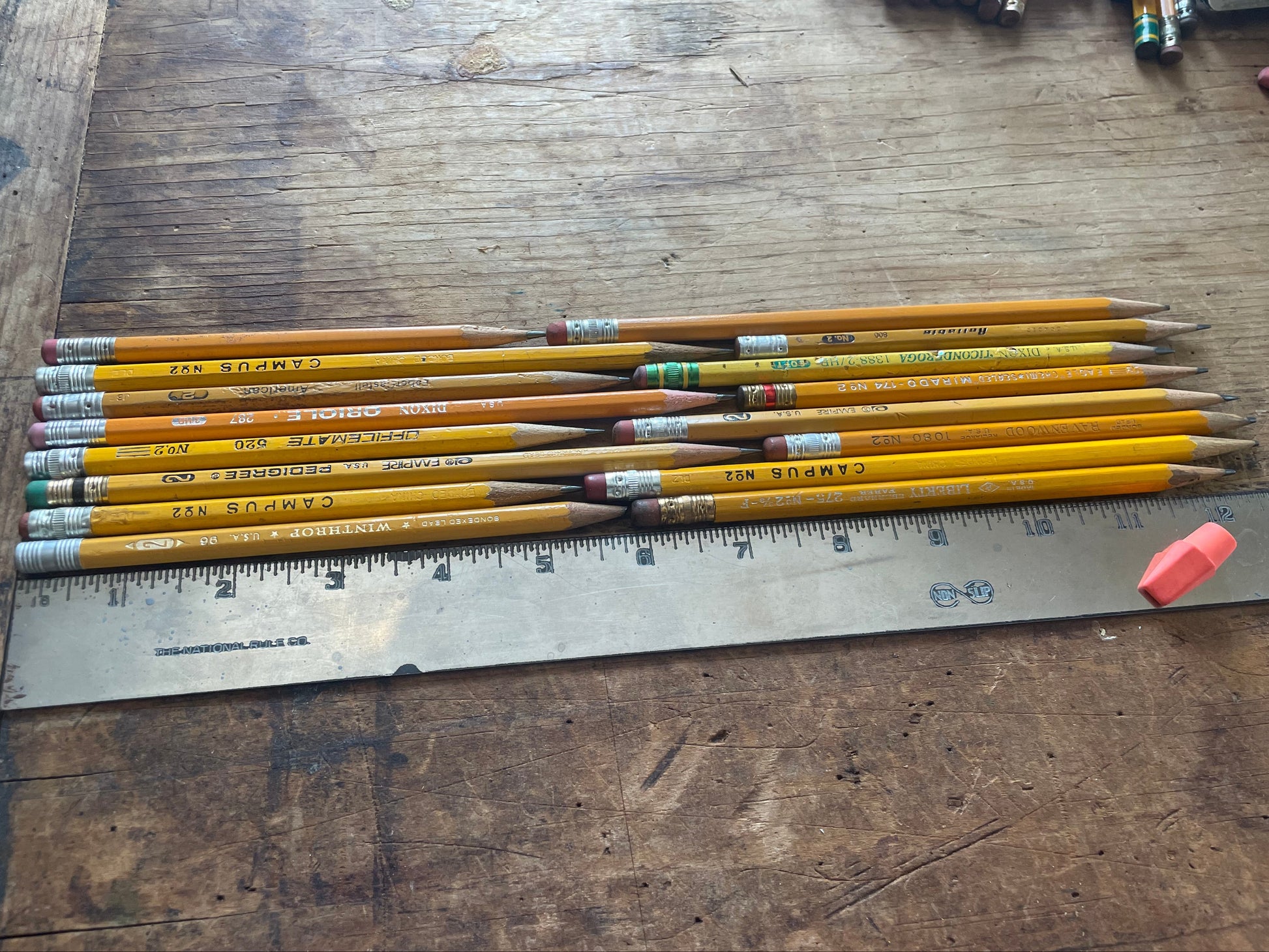 A group of yellow wooden pencils with erasers and erasers laid next to a metal ruler on a rustic wooden tabletop.