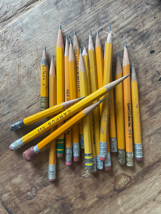 A pile of yellow school pencils with mixed metal ferrules and pink erasers arranged on a rustic wooden tabletop.
