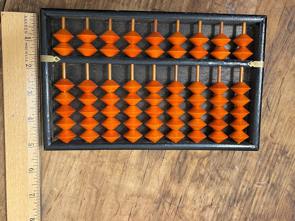 Vintage orange-and-black soroban abacus shown beside ruler for scale