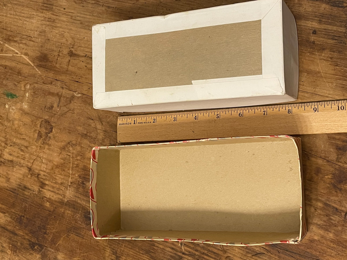 Open vintage presentation box with lid and cream interior beside ruler