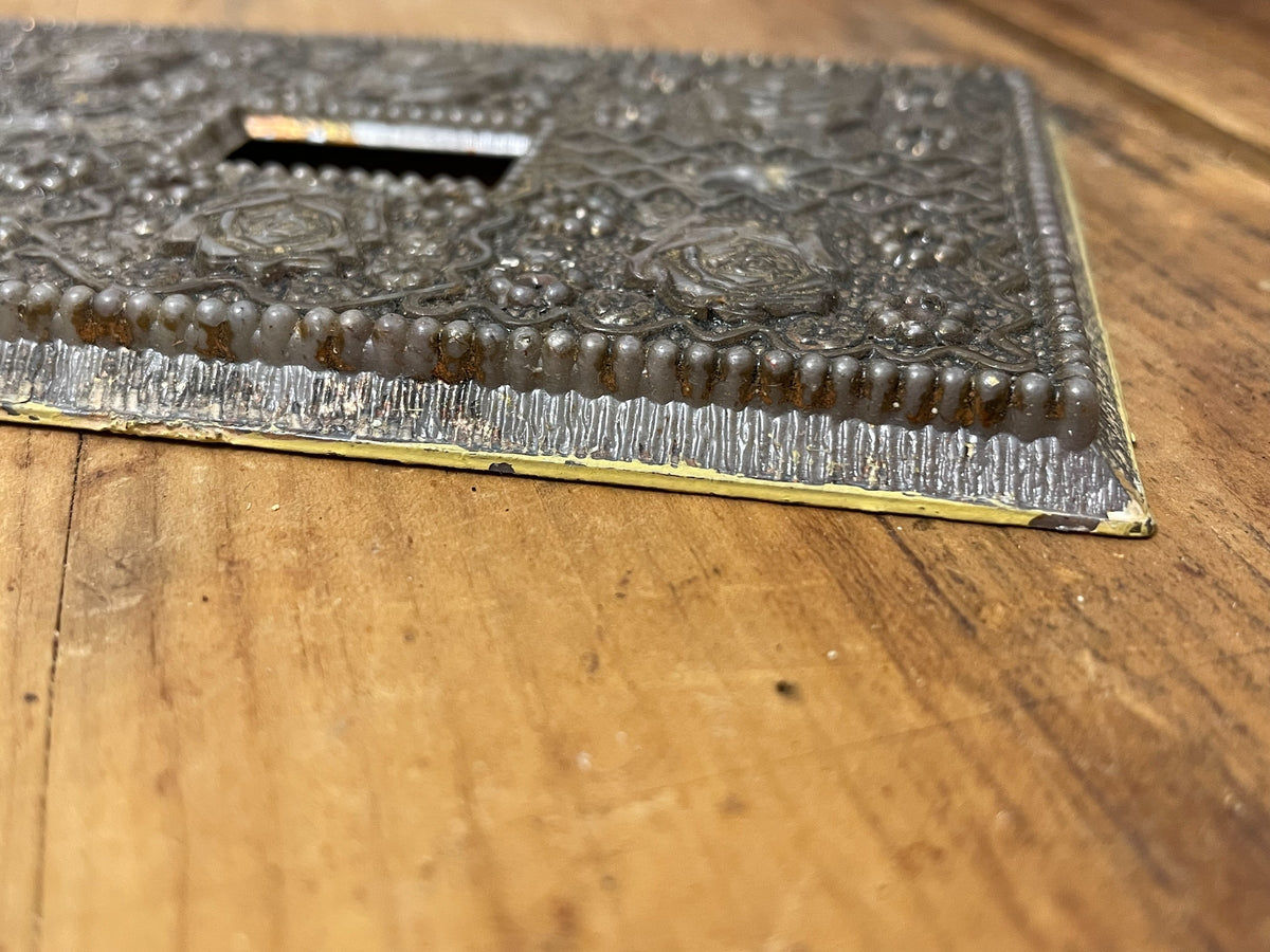 Close-up of ornate floral faux-silver surface on vintage plastic toggle switch plate