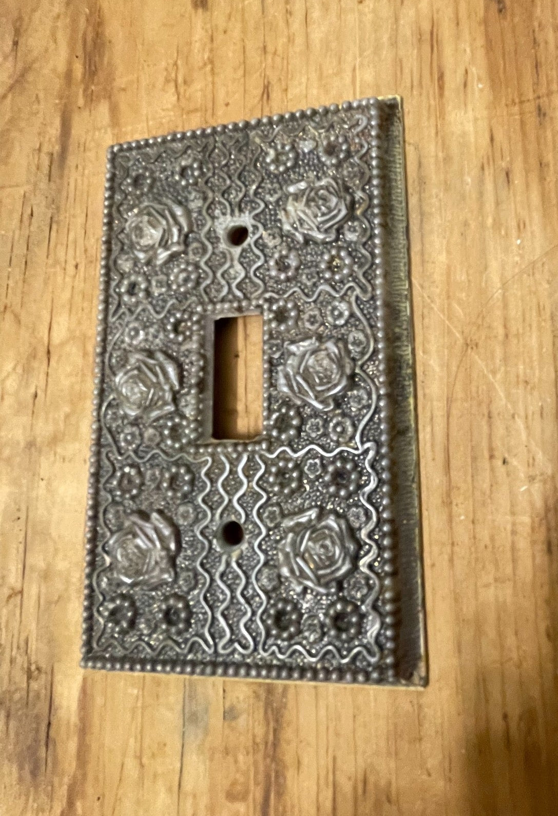 Full view of vintage ornate single-toggle switch plate on wood surface