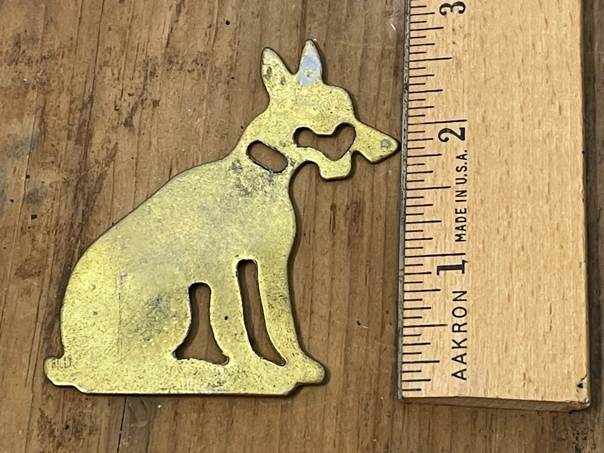 Brass-tone dog-shaped game piece beside ruler for scale