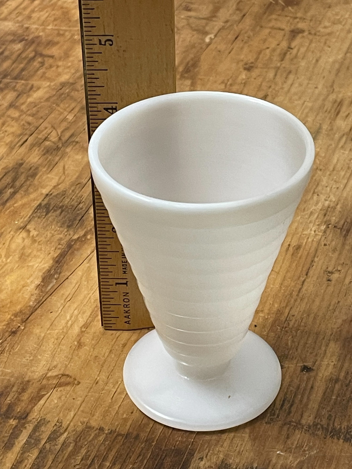 White milk glass footed cup beside ruler showing height