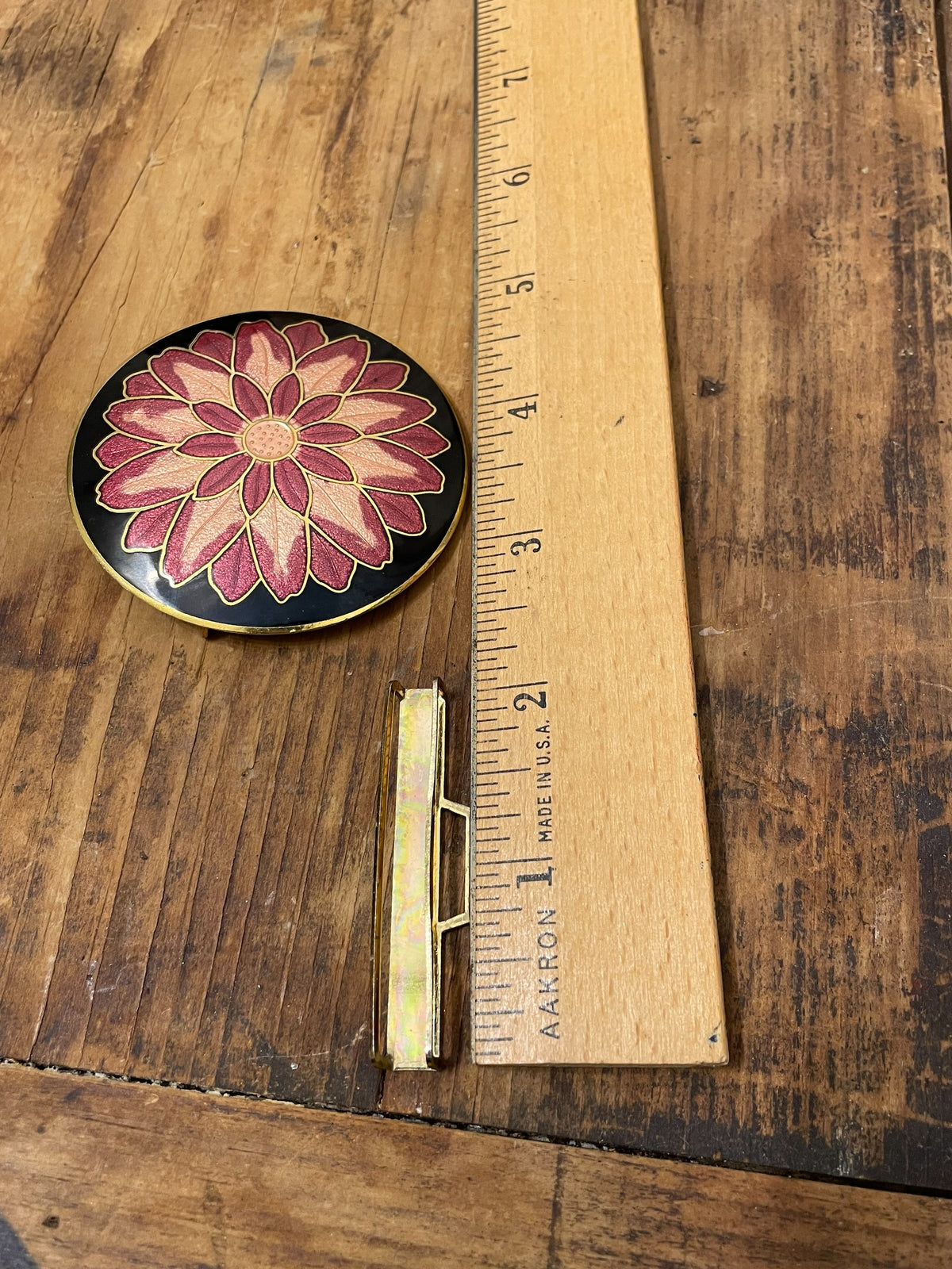 Round floral enamel belt buckle beside ruler showing scale