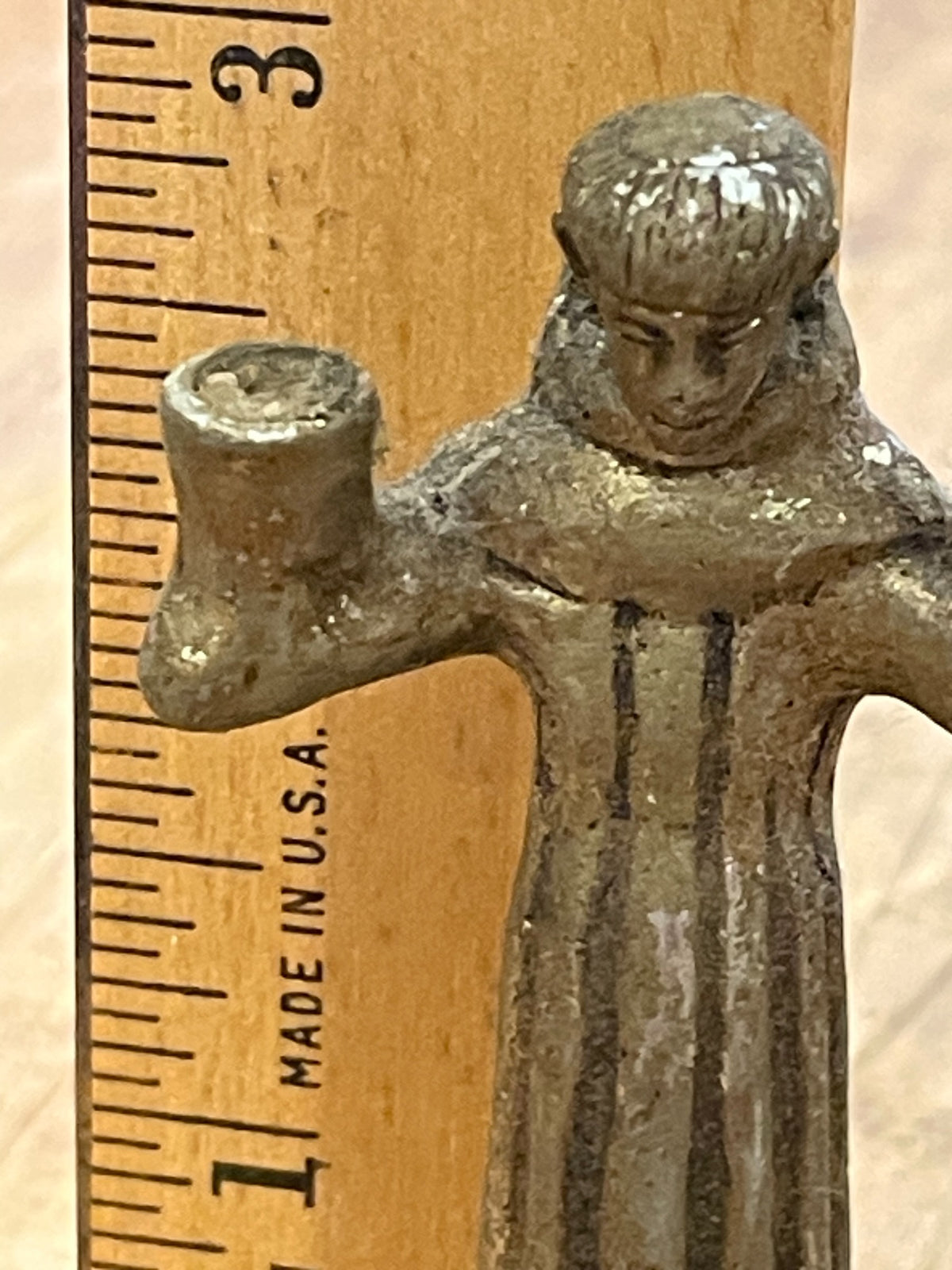 Small cast metal monk or saint figure beside ruler showing height