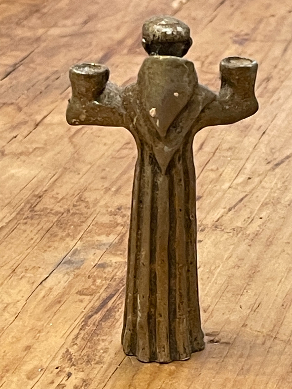 Back view of small cast metal robed figure with two candle sockets