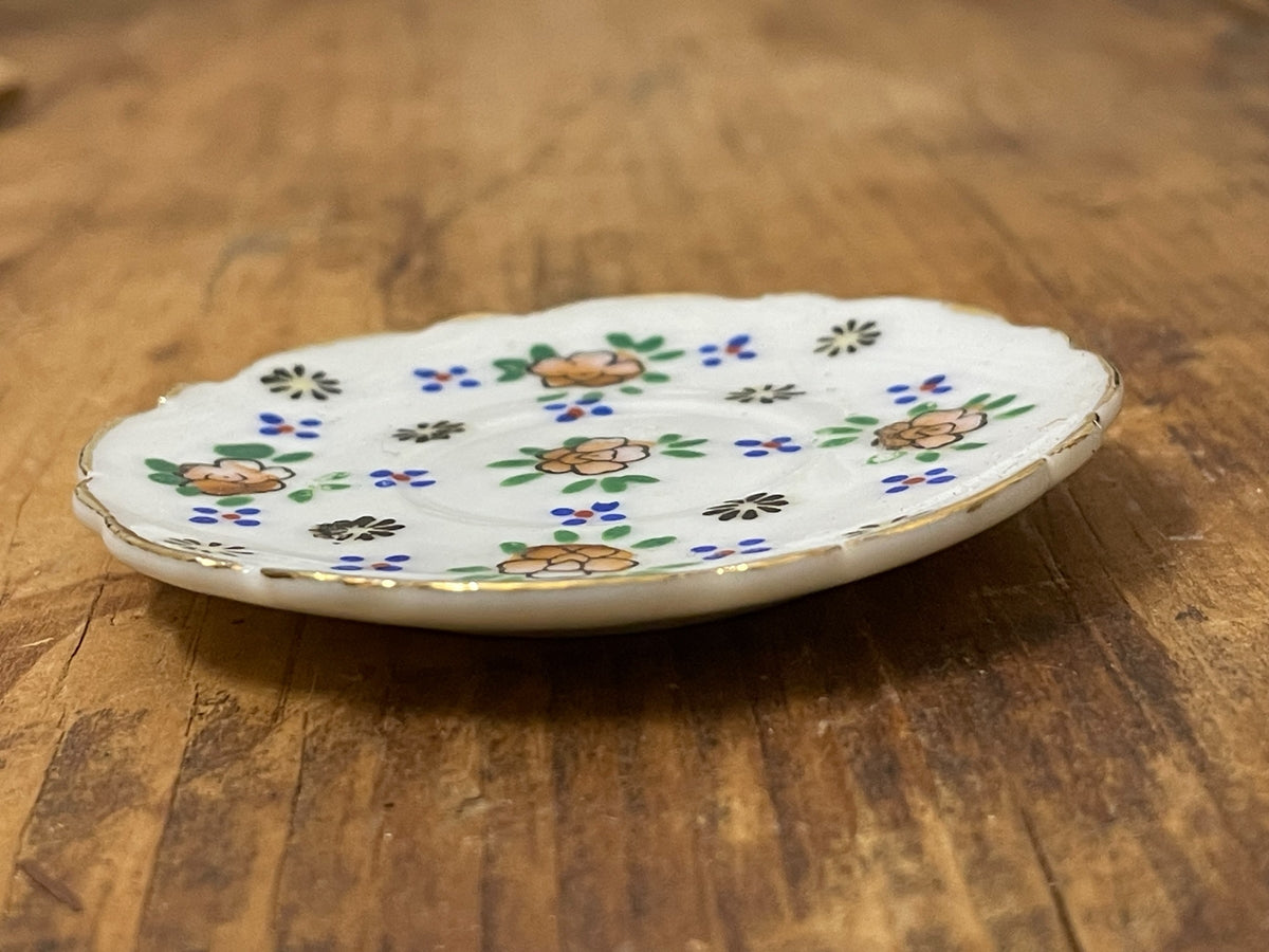 Side profile of miniature white porcelain floral plate with scalloped edge