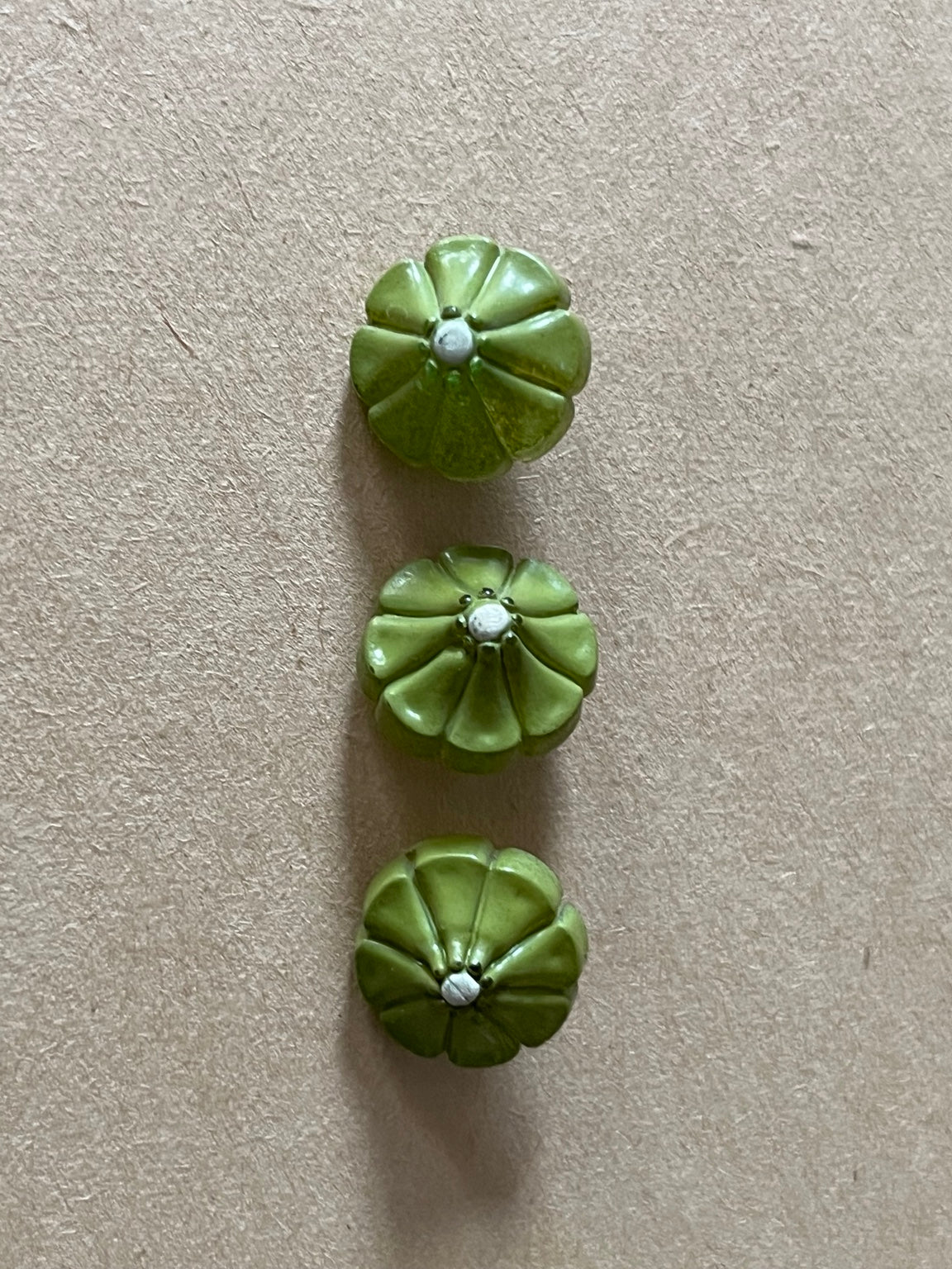 Three olive green flower-shaped buttons on beige paper.