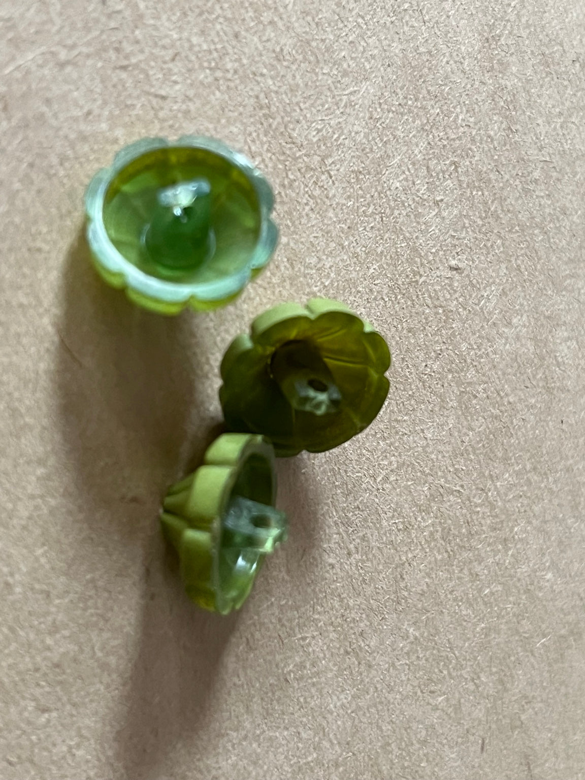 Three olive green flower-shaped buttons showing their shank backs on beige paper.