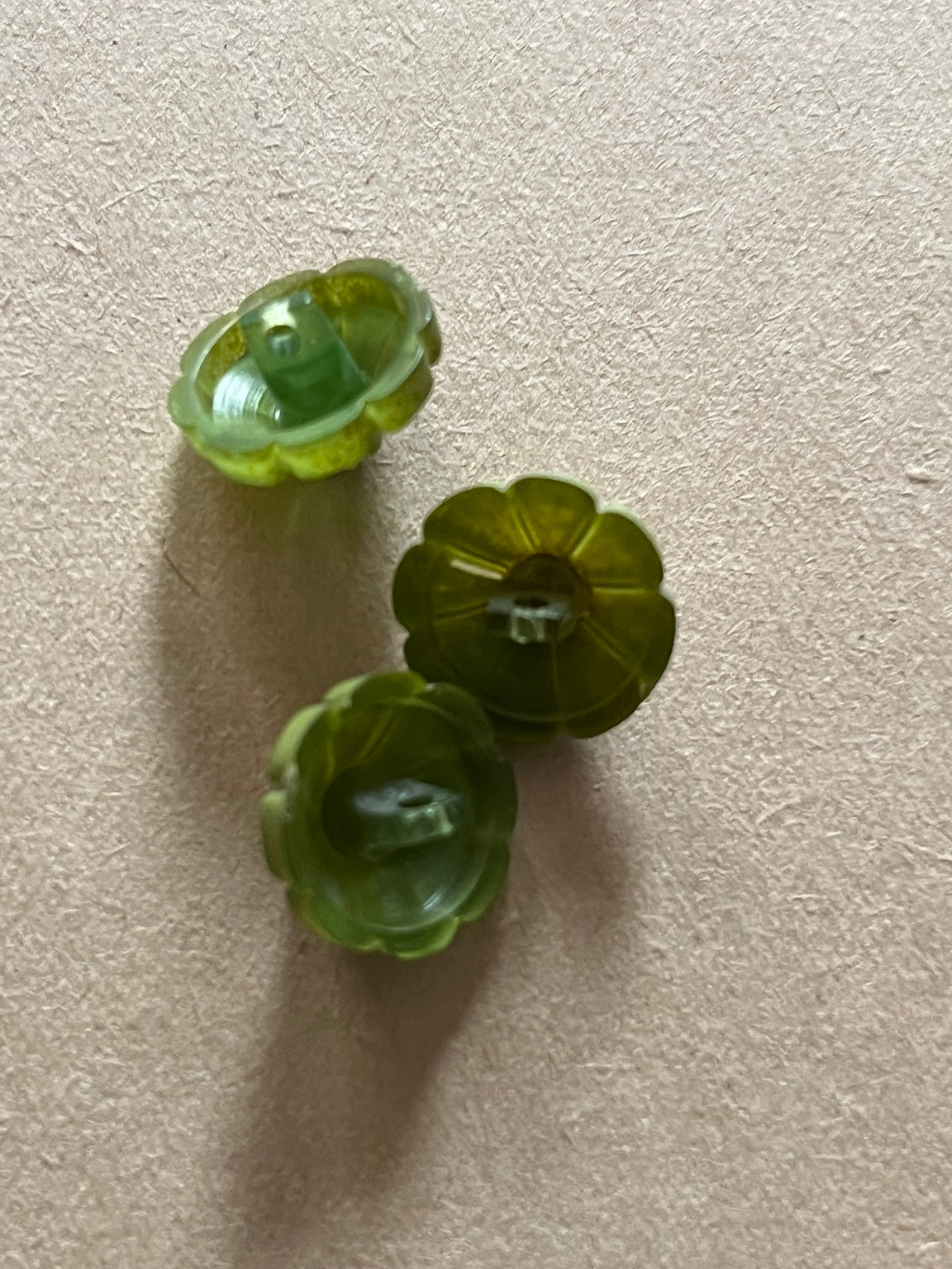 Three olive green flower-shaped buttons showing their shank backs on beige paper.