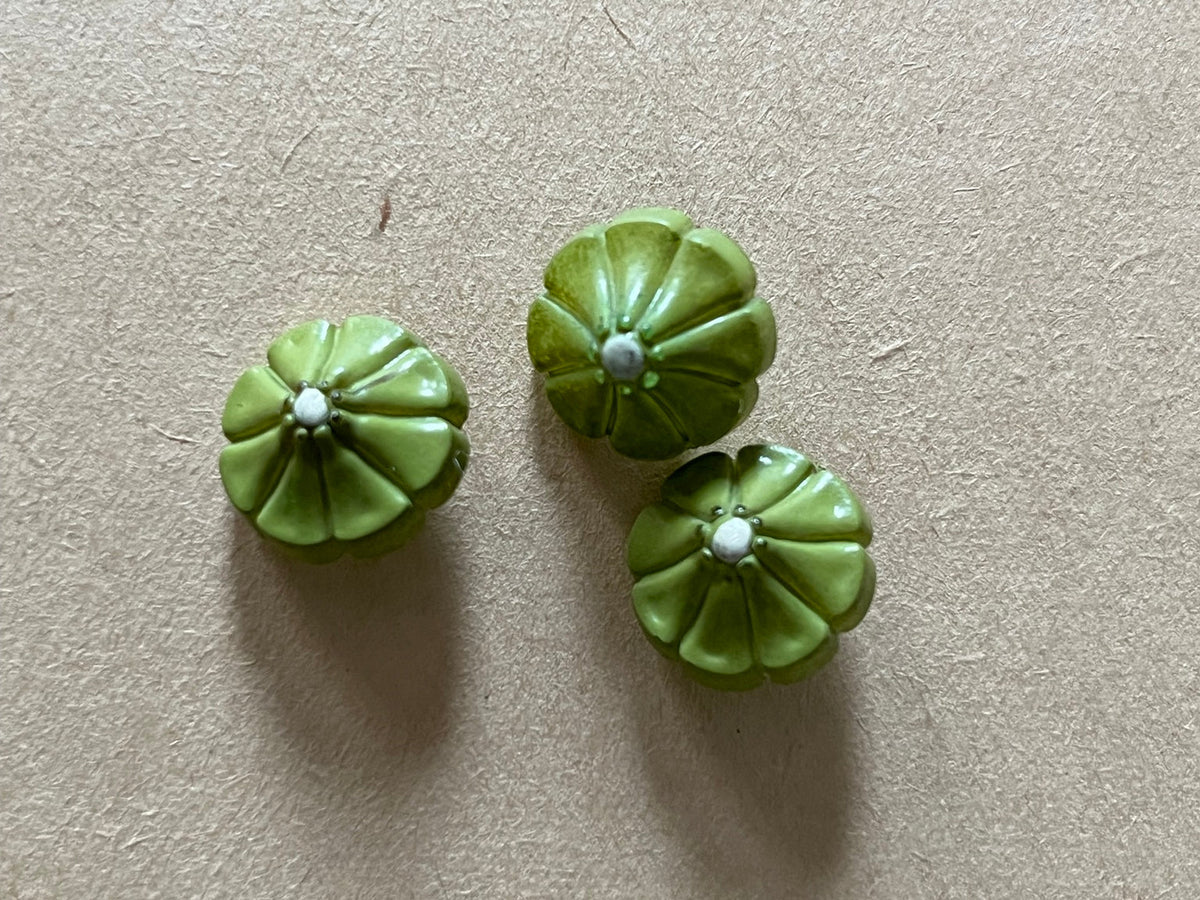 Three olive green flower-shaped buttons on beige paper.
