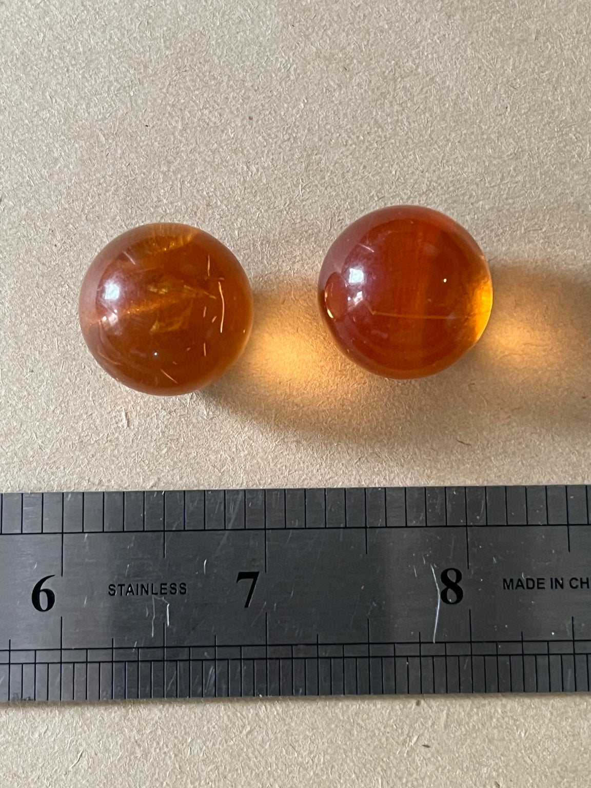 Two translucent amber-brown dome buttons beside a metal ruler on beige paper.