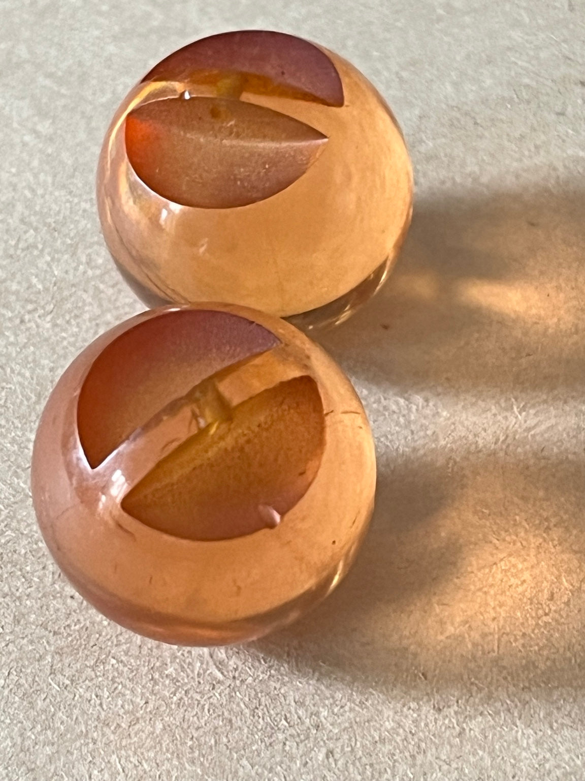 Two translucent amber-brown dome buttons showing slotted recessed backs on beige paper.