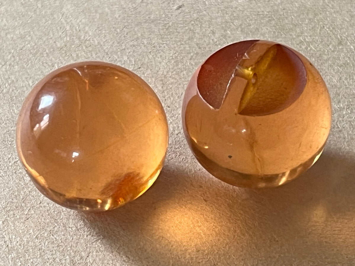 Two translucent amber-brown dome buttons showing front and slotted back on beige paper.