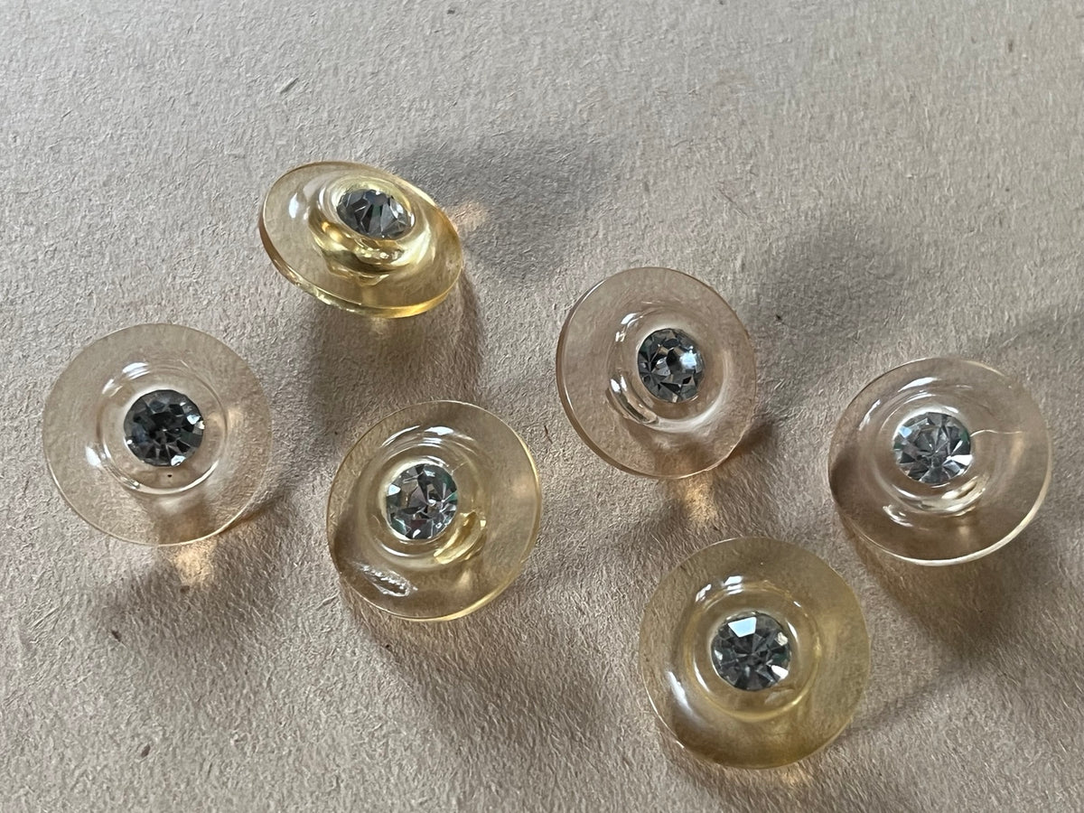 Six translucent pale champagne round buttons with clear faceted centers on beige paper.