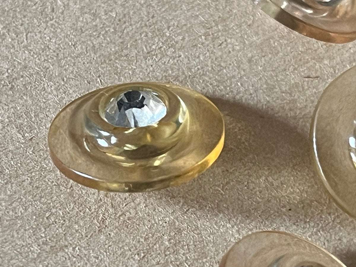 Six translucent pale champagne round buttons with clear faceted centers in a close-up on beige paper.