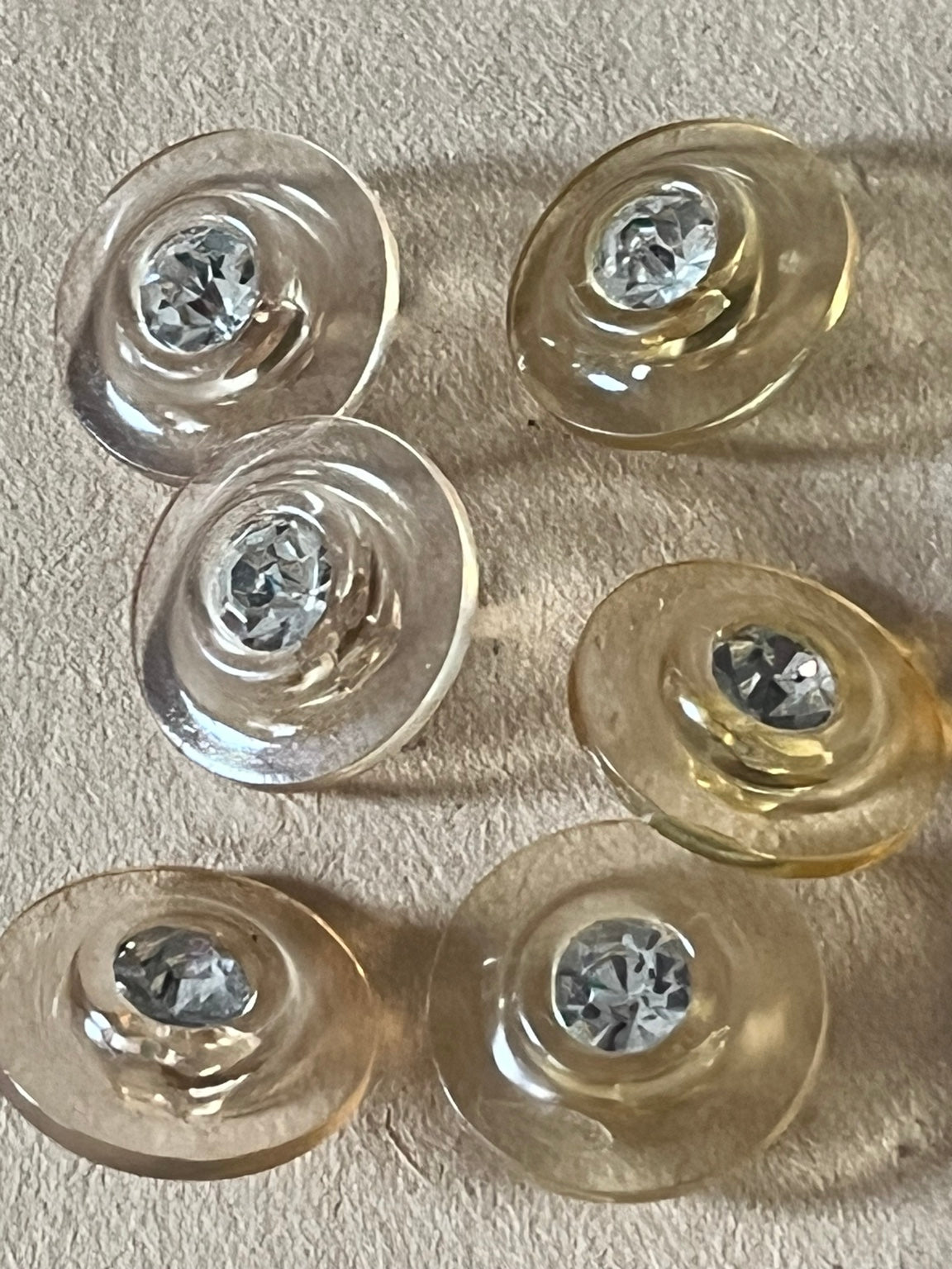 Six translucent pale champagne round buttons with clear faceted centers on beige paper.