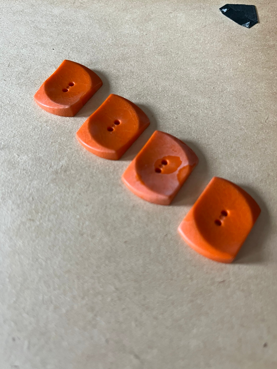 Four rust orange curved rectangular buttons showing recessed two-hole backs on beige paper.