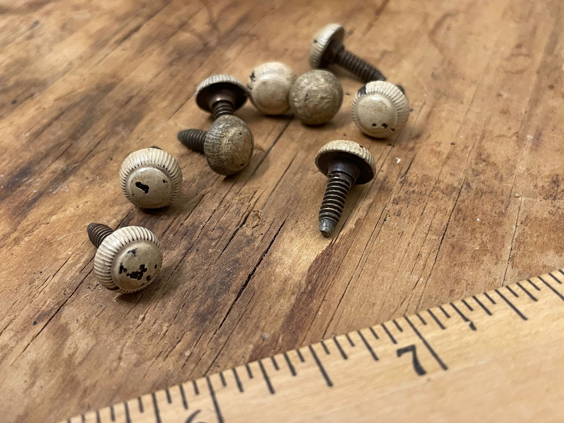 Set of nine antique screws with heavy patina o na wooden background with a wooden ruler in foreground