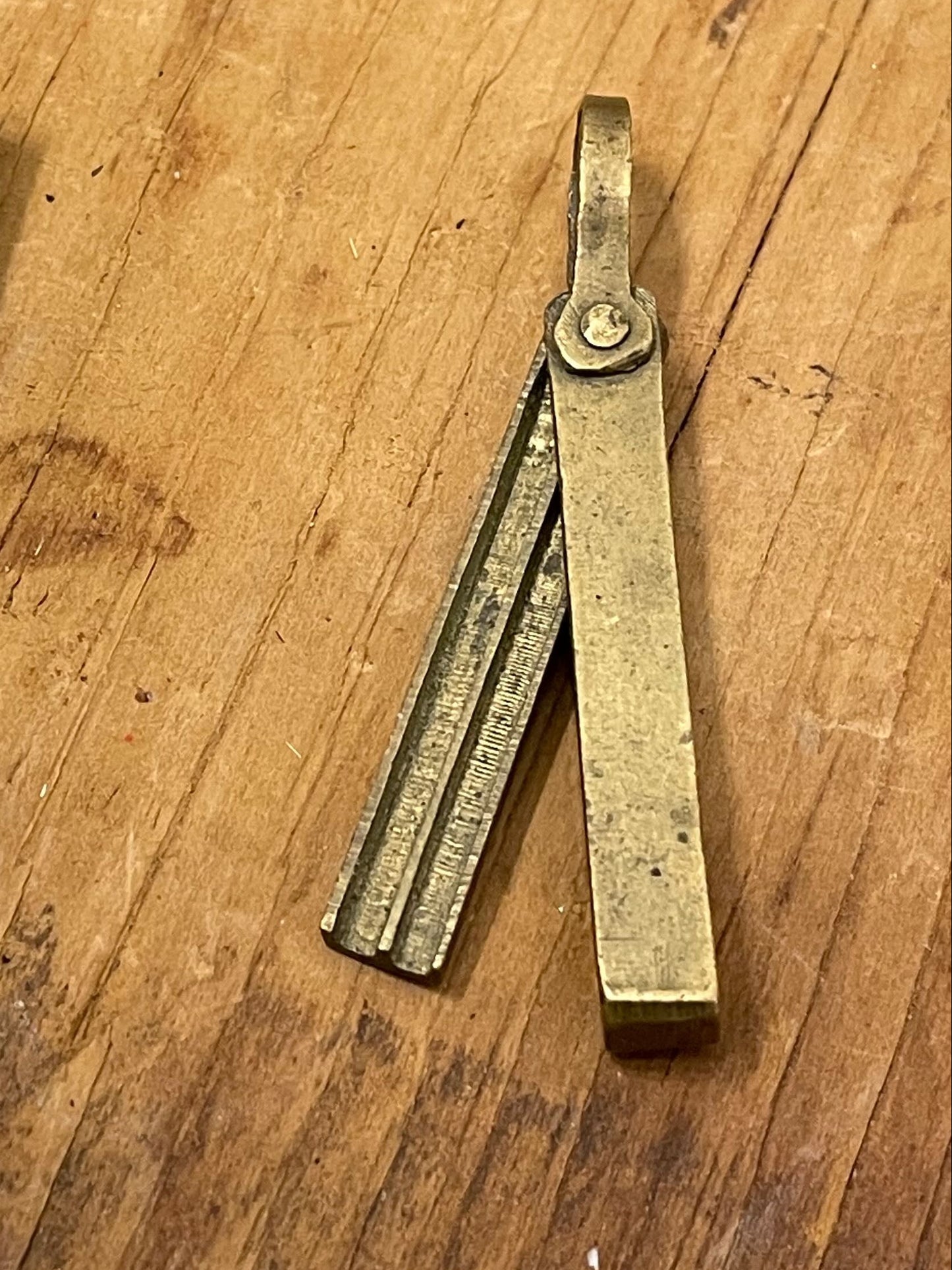 Petite brass pendant-style mechanical pencil lead holder on a wooden surface. 