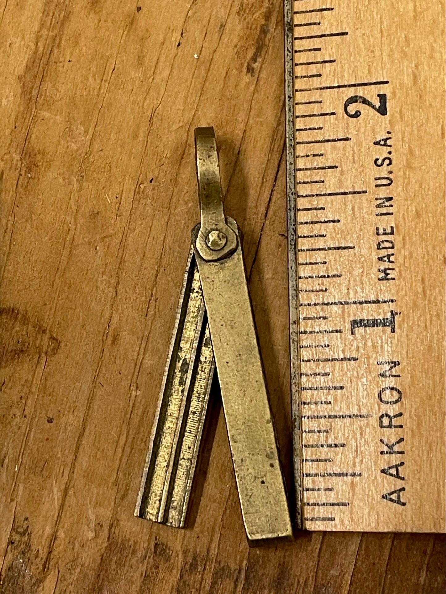Petite brass pendant-style mechanical pencil lead holder and a wooden ruler on a wooden surface (lead holder is roughly 1.75" long). 