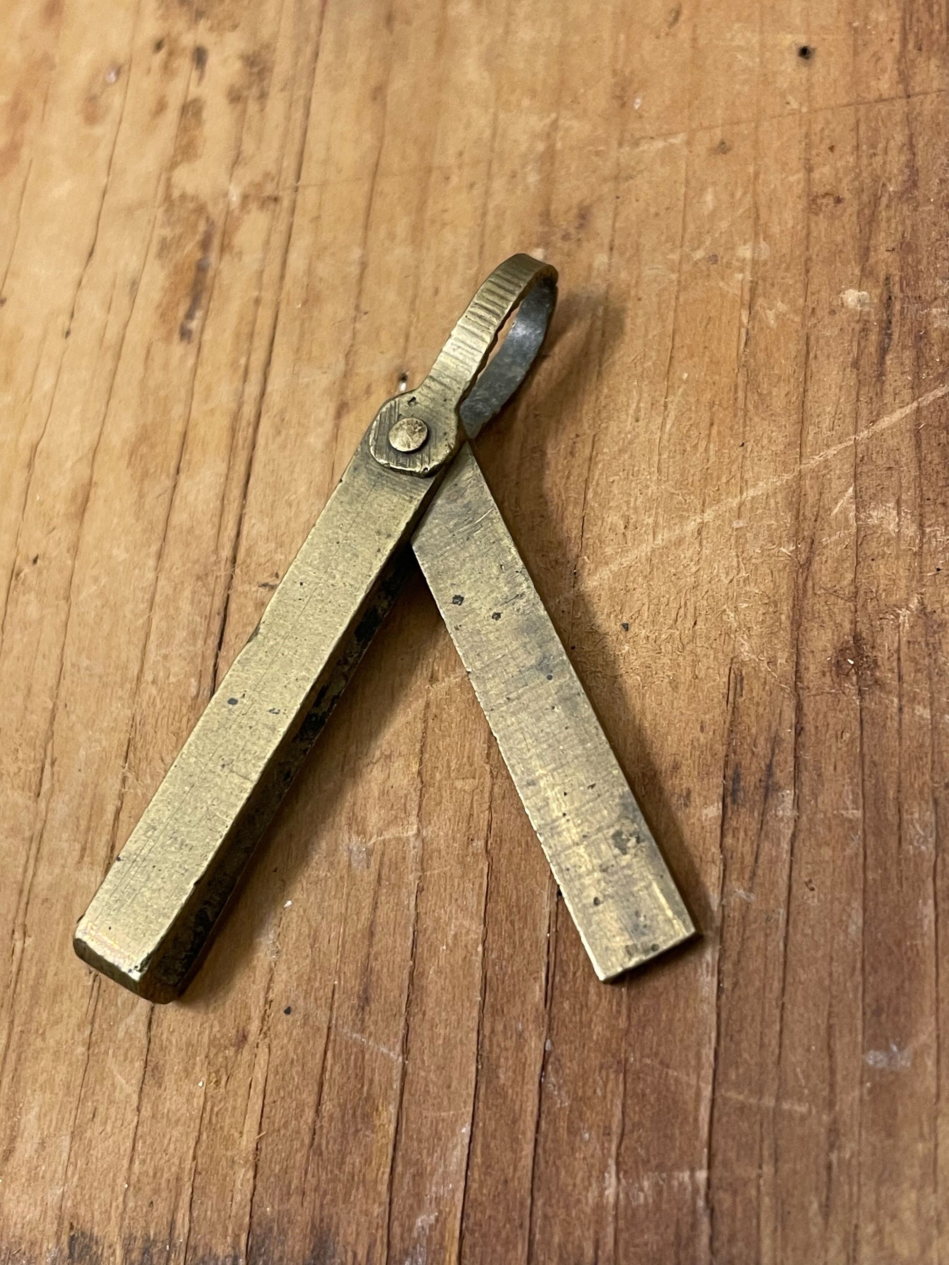 Petite brass pendant-style mechanical pencil lead holder on a wooden surface 