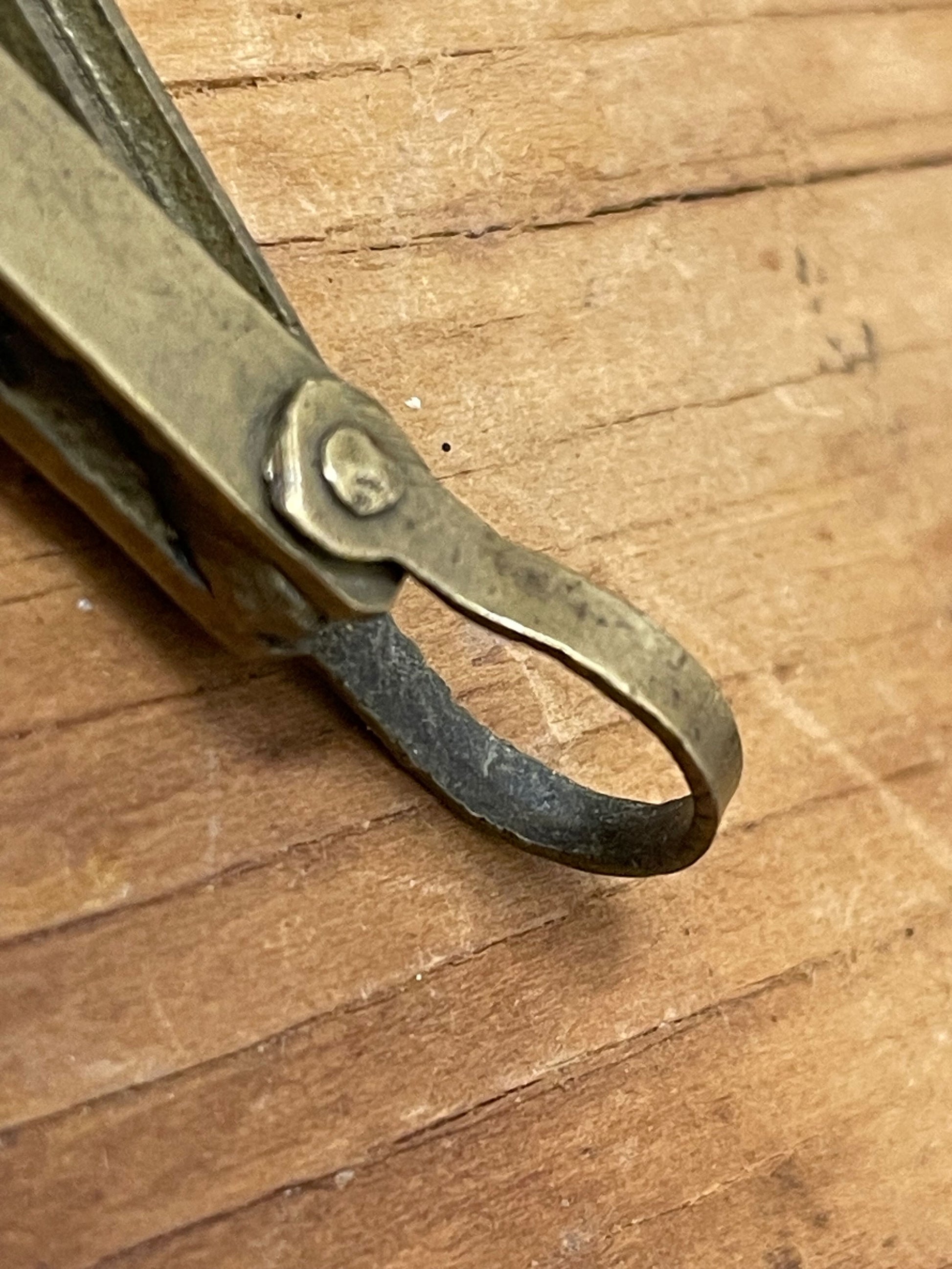 Closeup of the loop/pendant end of a petite brass pendant-style mechanical pencil lead holder on a wooden surface. 